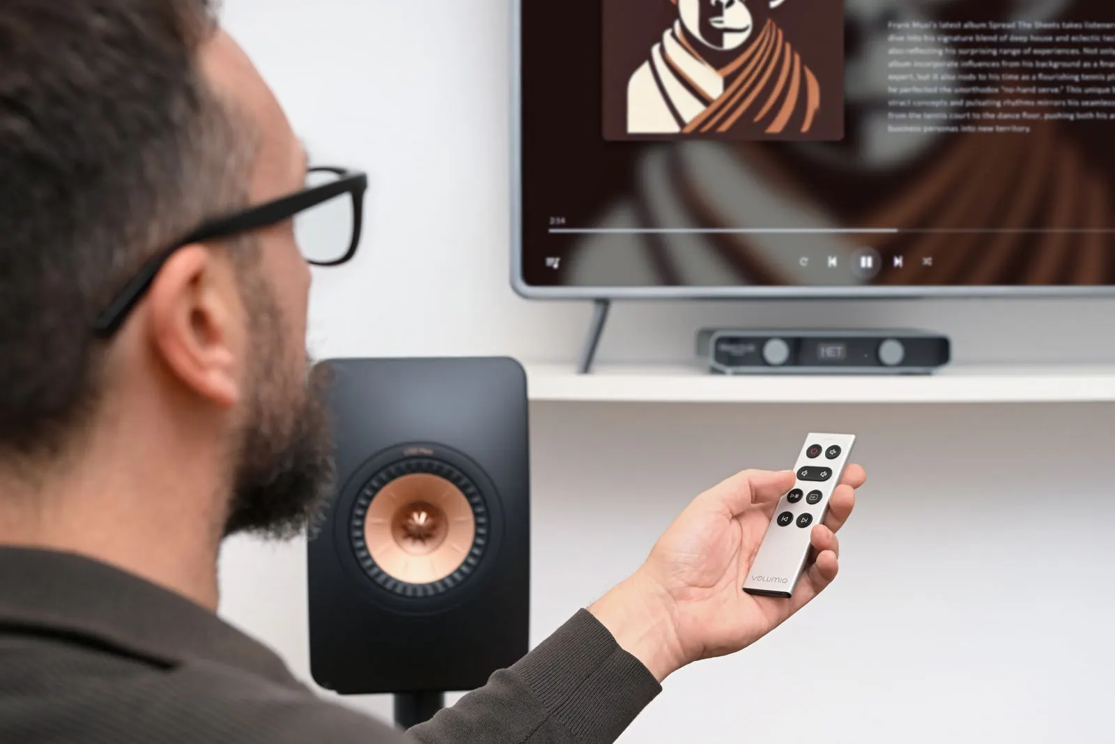 Una persona apunta con el mando Remoto a Primo Plus, con el televisor mostrando el álbum que suena.
