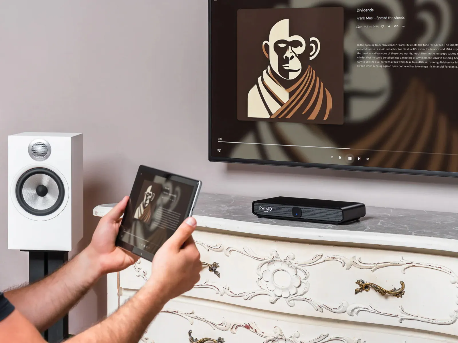 Una persona tiene in mano un tablet che mostra la copertina di un album, con Primo V3 su un cassettone e lo stesso album sulla TV sopra.