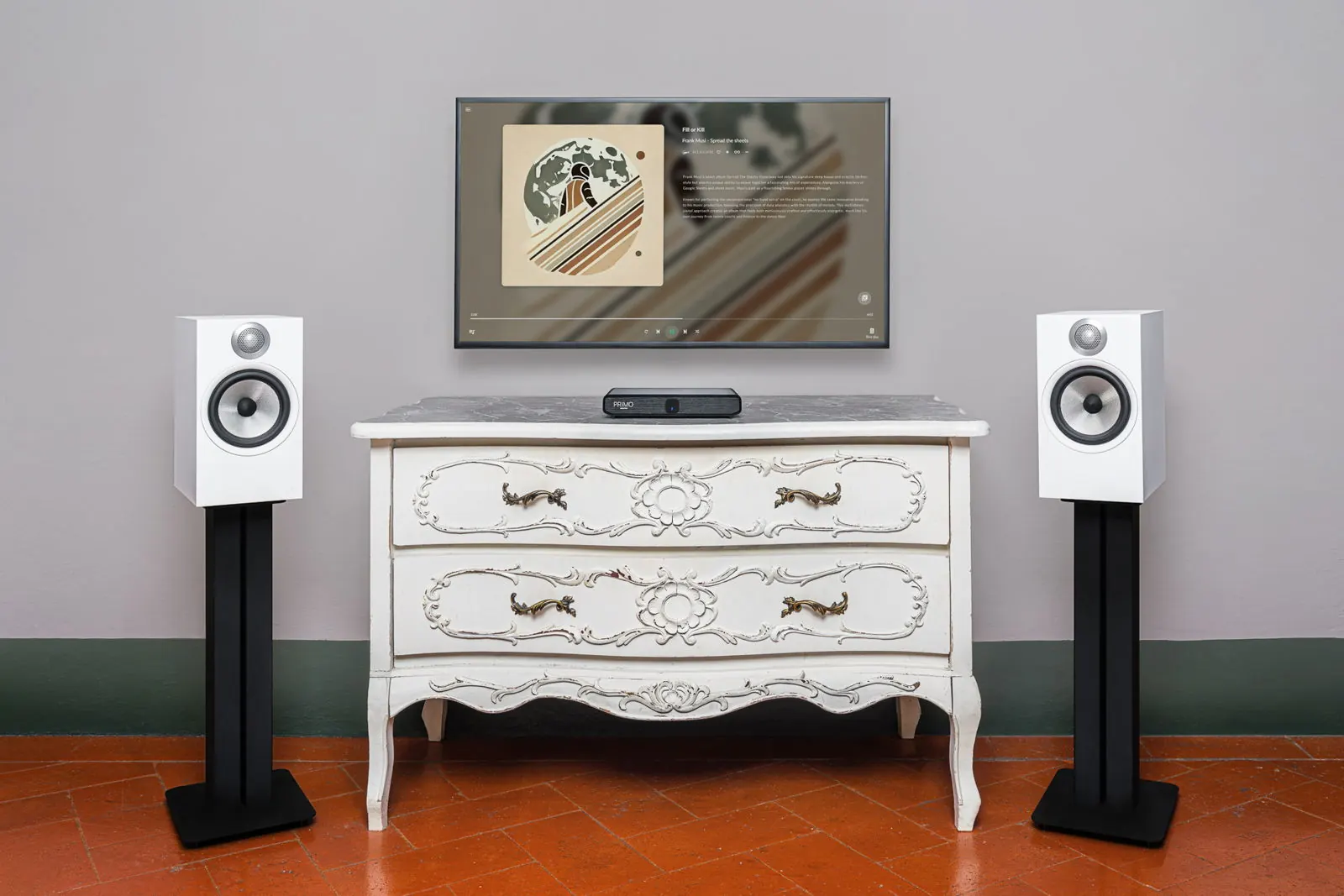 Un soggiorno con una TV a parete che mostra la copertina di un album, due diffusori bianchi sui supporti e Primo V3 su un cassettone bianco intagliato.