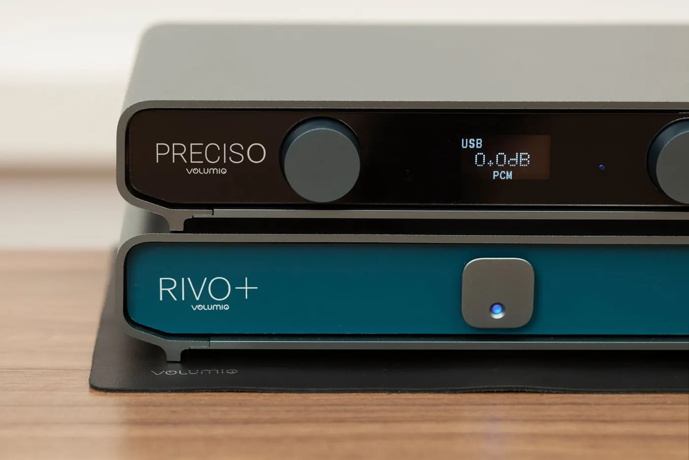 Preciso impilato sopra un Rivo Plus con frontale blu, su un tappetino nero su un tavolo di legno. Il display di Preciso mostra USB, 0.0dB e PCM.