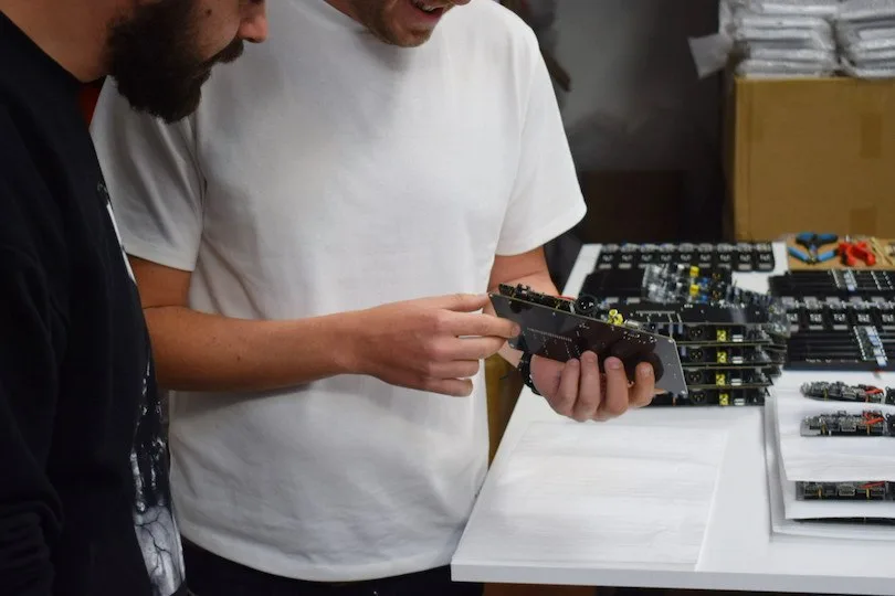 Two Volumio team members check a main board at the assembly table in Florence, with a stack of finished boards beside them.